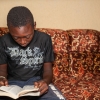 Sekouba kan godt lide at læse. Det er især bøger om andre lande, han er interesseret i. Her sidder han i familiens fine stue. Foto: William Vest-Lillesøe
